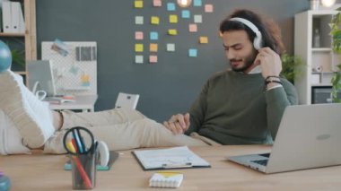 Modern ofiste kulaklıkla müzik dinleyen neşeli Arap işadamı