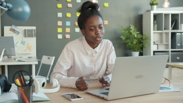 Cheerful Afro-American girl making online video call with laptop in workplace — Stock Video