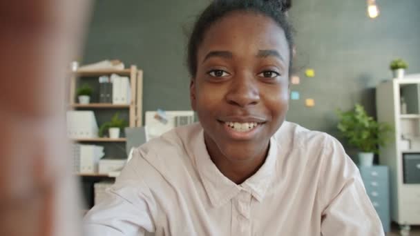 Retrato de la feliz joven dama de raza mixta hablando y agitando la mano mirando a la cámara en la oficina — Vídeos de Stock