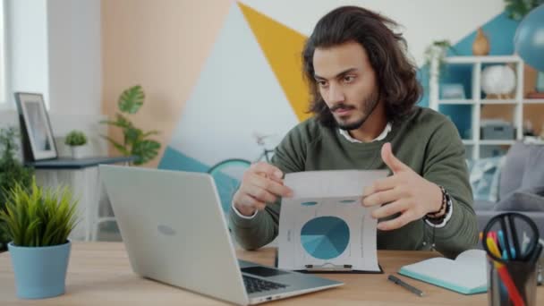 Αραβικός επιχειρηματίας που εργάζεται στο σπίτι κοιτάζοντας έγγραφα και χρησιμοποιώντας φορητό υπολογιστή — Αρχείο Βίντεο