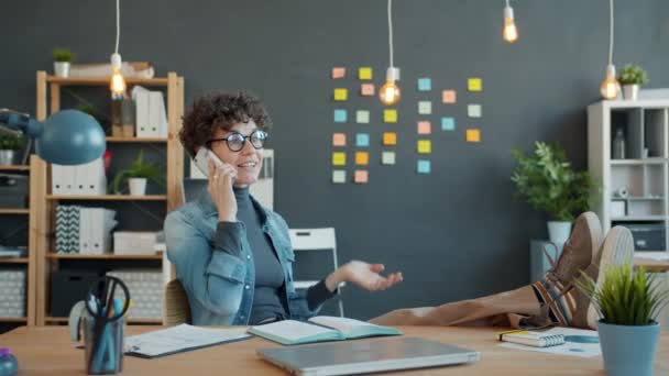 Neşeli genç bir kadın cep telefonuyla konuşuyor ve ofiste el kol hareketi yapıyor. — Stok video