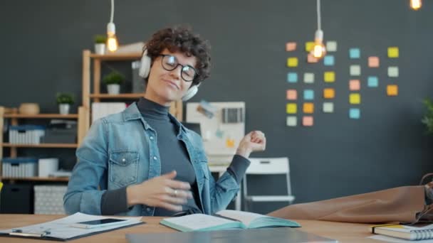 Gondtalan lány zenét hallgat és mozgó karok táncolnak az asztalnál a munkahelyen — Stock videók