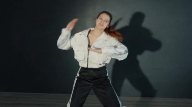 Spor elbiseli çekici bir genç, karanlık stüdyoda dans ediyor.