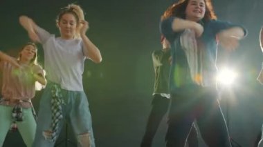 Yaratıcı dansçıların yavaş çekimde kapalı alanda aydınlanmış sahnede havalı dans gösterileri.