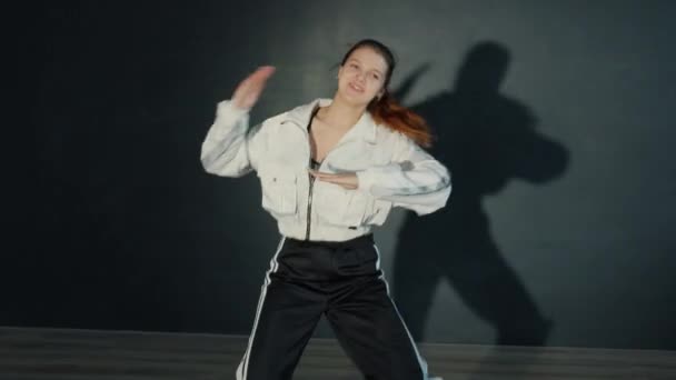 Aantrekkelijke tiener in sportkleding dansen in donkere studio met verlichting — Stockvideo