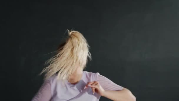 Młoda kobieta z kucykiem tańcząca w ciemnym holu patrząc w kamerę — Wideo stockowe