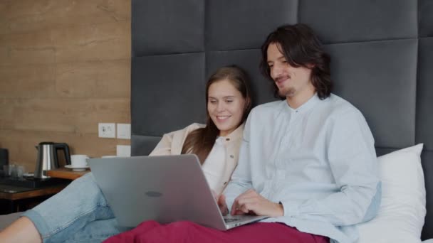 Hombre y mujer usando computadora portátil y hablando en la cama en la habitación de hotel — Vídeos de Stock