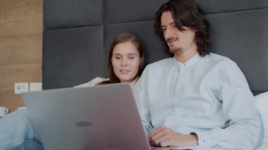 Kız ve erkek yatakta dizüstü bilgisayar kullanıyor ve online içeriği tartışıyorlar.
