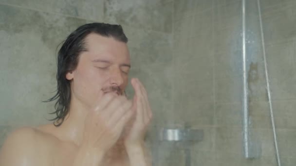 Jóképű fiatal, hosszú hajú férfi mossa az arcát és a haját, miközben otthon zuhanyzik. — Stock videók