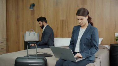 İş adamları, otel odasında bilgisayarlı ve akıllı telefonlu cihazlarla çalışıyor.