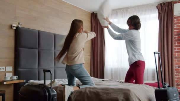 Szczęśliwy młody para walki poduszki i śmiech zabawy w pokoju hotelowym — Wideo stockowe