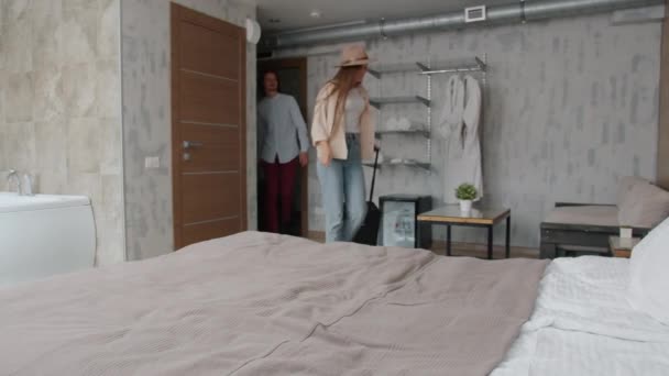 Муж и жена туристов, входящих в гостиничный номер падает на кровать улыбаясь наслаждаясь отдыхом — стоковое видео