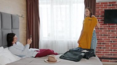 Genç bir kadın otel odasında giysilerini çıkarıp poz verirken, bir adam da akıllı telefonuyla fotoğraf çekiyor.