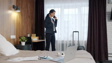 Takım elbiseli mutlu kız otelden arıyor cep telefonuyla konuşuyor ve gülümsüyor.