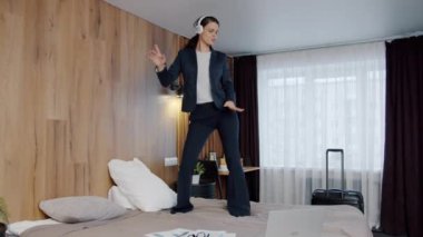 Otel yatağında dans eden güzel iş kadını kulaklık takıp eğleniyor.