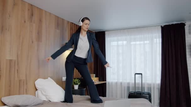 Slow motion av glada affärskvinna dans på sängen på hotellet lyssna på musik via hörlurar — Stockvideo
