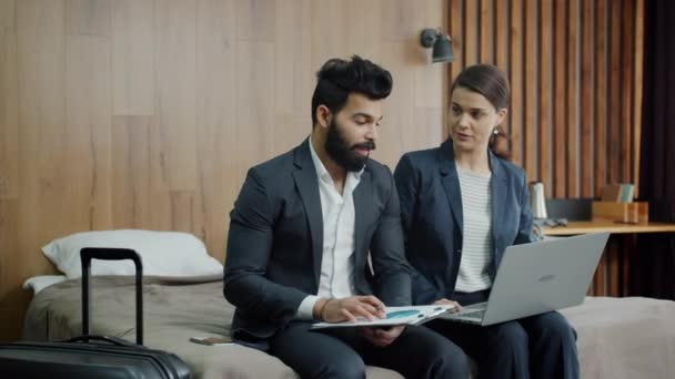 Dziewczyna i facet w garniturach rozmawiają patrząc na ekran laptopa w nowoczesnym pokoju hotelowym — Wideo stockowe