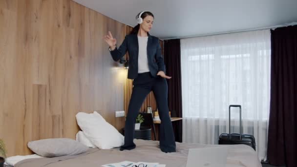 Piękna bizneswoman tańcząca na łóżku hotelowym bawiąc się w słuchawki — Wideo stockowe