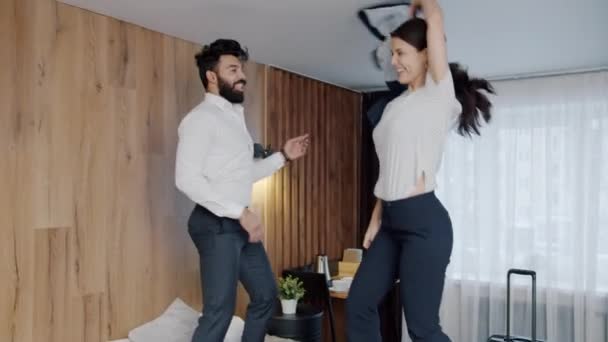 Радостные молодые люди муж и жена танцуют на кровати отеля раздеваясь весело — стоковое видео