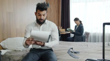 Kadın arka planda kitap okurken, işadamının oteldeki gazetelere bakması ağır çekim