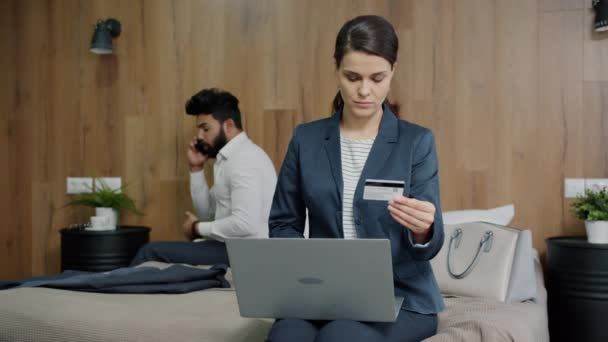 Γυναίκα κάνει online πληρωμή με τραπεζική κάρτα και laptop, ενώ ο άνθρωπος μιλάει στο κινητό τηλέφωνο στο ξενοδοχείο — Αρχείο Βίντεο