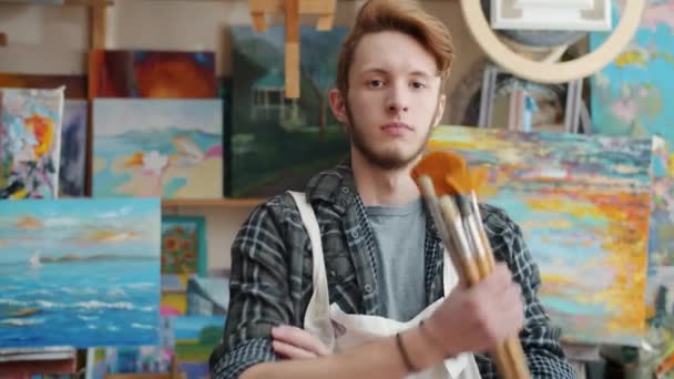 Portret van een creatieve jonge schilder in de kunstklas met penselen — Stockvideo