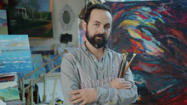 Портрет доброзичливого художника, що стоїть в студії, що тримає пензлі — стокове відео