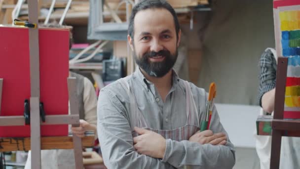 Portret van kunstleraar volwassen man glimlachend in de klas terwijl studenten schilderen op de achtergrond — Stockvideo
