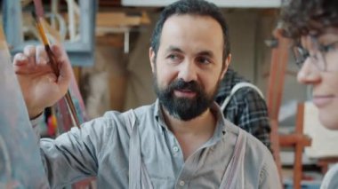 Resim öğretmeni ve öğrencilerin atölyedeki resimlere bakarak tartıştığı portre