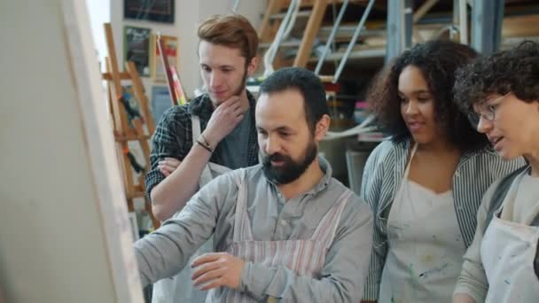 Feliz grupo de jóvenes mili-étnicos hablando con el profesor de artes y riendo durante la clase en el estudio — Vídeos de Stock