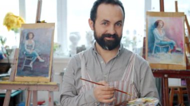 Sanat stüdyosunda palet ve boya fırçası tutan yakışıklı bir adamın portresi.