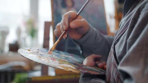 Primer plano en cámara lenta de artistas masculinos mezclando a mano los colores de pintura en la paleta y luego pintando la imagen — Vídeos de Stock