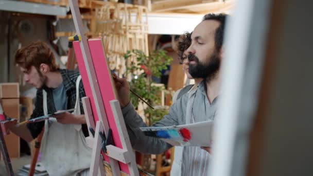 Досвідчена художниця показує молодій леді, як малювати картини, що викладають в студії — стокове відео