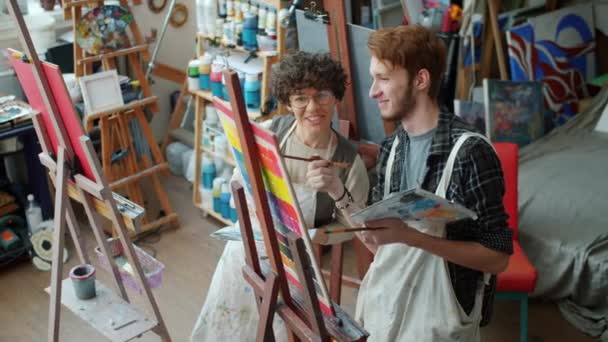 Man en vrouw kunstenaars in gesprek kijken naar beeld op ezel bespreken kunstwerk in studio — Stockvideo