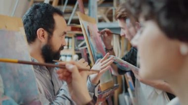 Orta yaşlı esmer sanat öğretmeninin sınıfta resim çizen öğrencilerle konuşması yavaş çekimde.