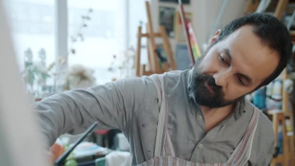 Portret van knappe man van middelbare leeftijd kunstenaar schilderij schilderij werken in workshop alleen — Stockvideo