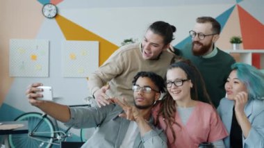 Neşeli iş arkadaşları ofiste akıllı telefon kamerasıyla selfie çekiyorlar.