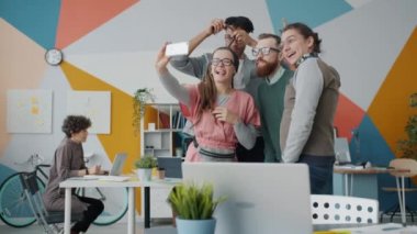 Neşeli gençlik ofiste eğleniyor, selfie çekiyor ve akıllı telefon kamerasıyla gülüyor.
