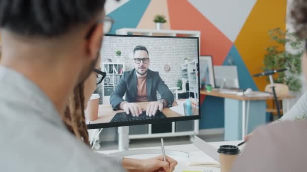 Jovem conversando com grupo de colegas online através de videochamada no escritório — Vídeo de Stock