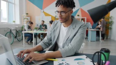 Bilgisayarda yazı yazan ve gülümseyen mutlu Afro-Amerikalı adam ofiste iş iletişiminden keyif alıyor.