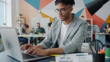 Laptop kullanan ciddi bir Afro-Amerikalı. Sonra da modern ofiste çalışan notlar yazıyor.