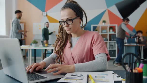 Rallentatore di giovane donna che utilizza il computer mentre i colleghi lavorano e si divertono in ufficio — Video Stock