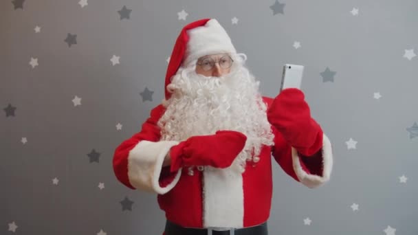 Санта Клаус с помощью смартфона делает селфи позируя в красном костюме и шляпе — стоковое видео
