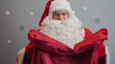 Noel Baba kostümü giymiş bir adamın portresi kollarını bavulla kameraya uzatıyor.
