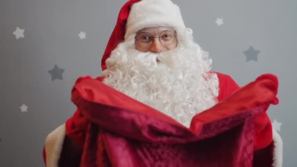 Retrato de hombre en traje de Santa ofrenda presenta brazos extendidos con bolsa a la cámara — Vídeos de Stock