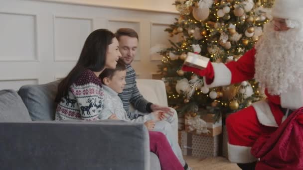 Babbo Natale si congratula con la famiglia felice dando scatole regalo a madre e bambino in appartamento — Video Stock