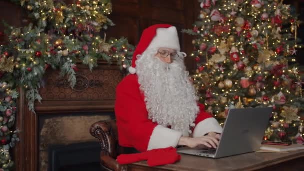 Santa em traje e óculos digitando carta com computador portátil em quarto decorado — Vídeo de Stock