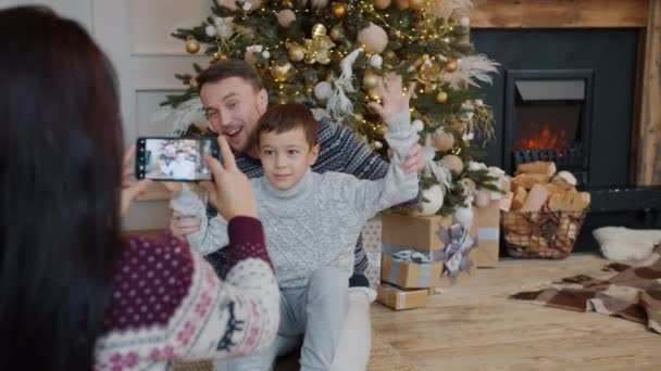 Ojciec i syn pozowanie do aparatu smartfona, podczas gdy matka robi zdjęcia w Wigilię — Wideo stockowe