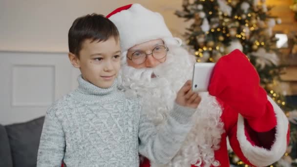 Santa i mały chłopiec podejmowania rozmowy wideo online za pomocą nowoczesnego smartfona rozmowy w pomieszczeniach — Wideo stockowe