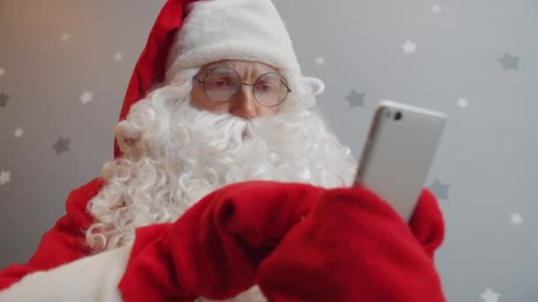 Чоловік у традиційному костюмі Санта, що витирає екран смартфона та зворушливі окуляри — стокове відео
